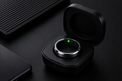 Un primer plano del Vera Ring™ | Monitorea tu Salud 24/7 desde tu Dedo, con luz LED verde, en su estuche de carga negro junto a un smartphone; perfecto para monitor de presión arterial y análisis del sueño.